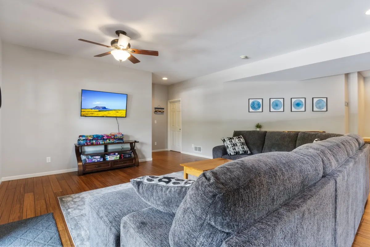 A spacious living room with a comfortable sectional sofa, a large flat-screen television mounted on the wall, a wooden coffee table, and decorative wall art. The mood is cozy and welcoming, fostering relaxation and group connection.