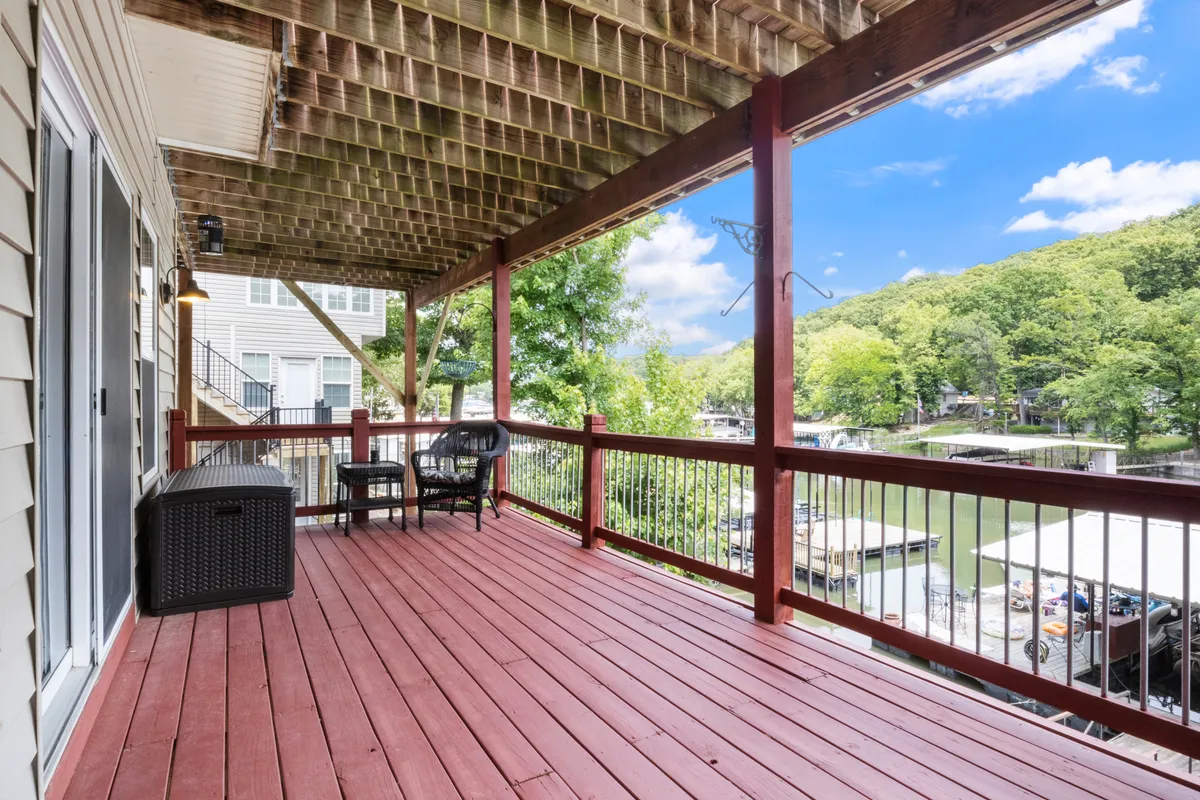 A spacious wooden deck overlooking the tranquil lake, featuring comfortable outdoor seating arranged to capture the stunning water views. The scene radiates relaxation, with soft light hinting at either early morning or golden hour, inviting guests to drink in the panorama and enjoy peaceful moments outdoors.