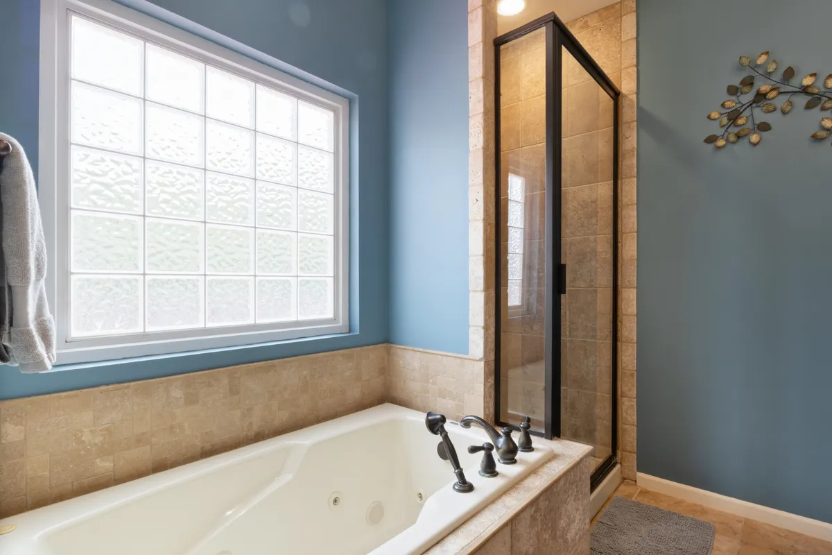 A serene bathroom featuring a large bathtub, shower enclosure, and window for natural light. The space is designed for soothing baths and refreshing showers, providing a perfect setting for unwinding after a long day.