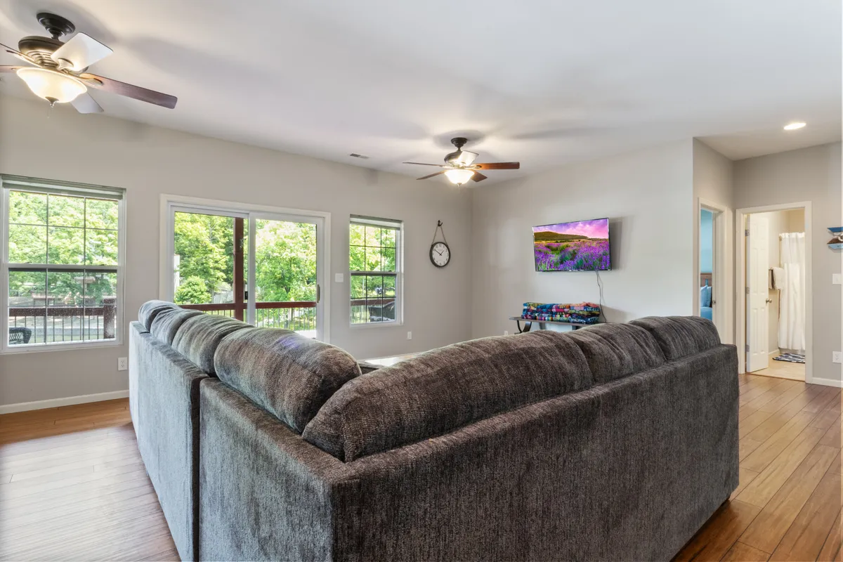 This image showcases a large sectional sofa facing windows that look out onto lush greenery, with a wall-mounted TV and a clock completing the scene. The light-filled space provides a sense of openness and the promise of restful moments after lively excursions.
