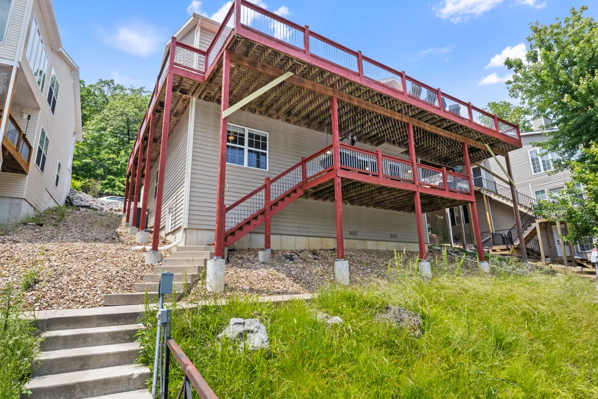 A large multi-level deck featuring a staircase and natural landscaping. The expansive space is suited for group activities, outdoor dining, and socializing in the sun or under the stars, providing a versatile area for events.