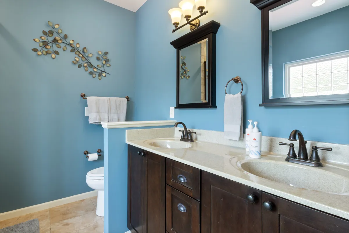 A modern, inviting bathroom with dual sinks, elegant mirrors, and decorative wall art. The space feels serene and spa-like, ideal for morning rituals or winding down with a relaxing bath.