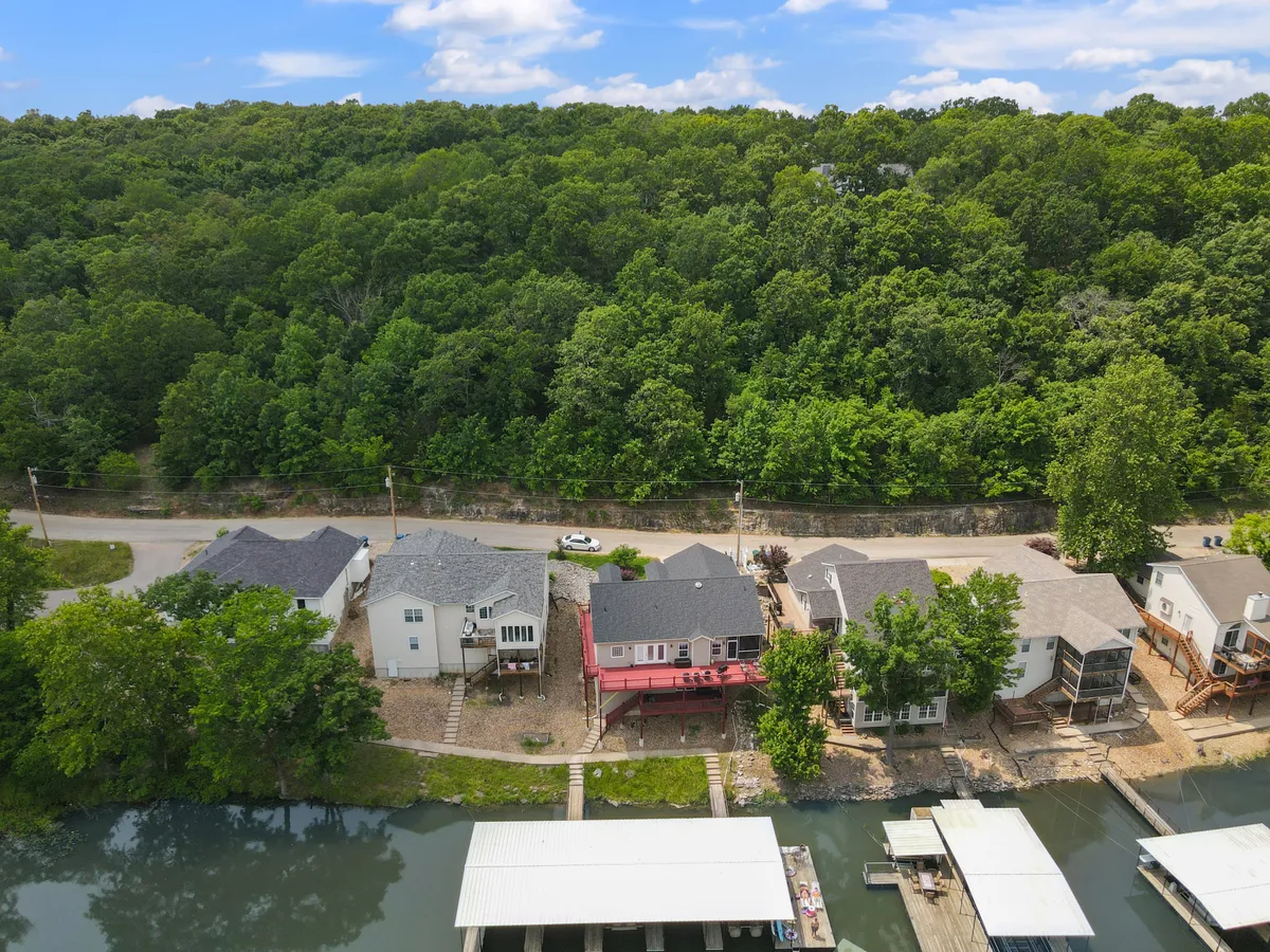 The image showcases waterfront properties lined along a tree-covered hillside, with a clear view of a boathouse and dock extending into the water. The tranquil atmosphere invites thoughts of boating, fishing, and enjoying water activities as part of daily life.
