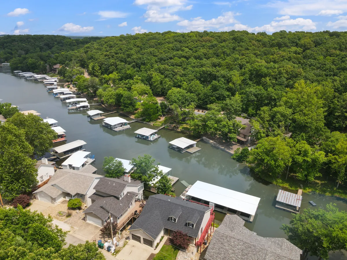 A scenic view of houses lining the waterway with boats docked along the shore, lush greenery surrounding the area, and a winding river leading off into the distance. The image radiates tranquility while also highlighting active lake life with visible watercraft and accessible docks.