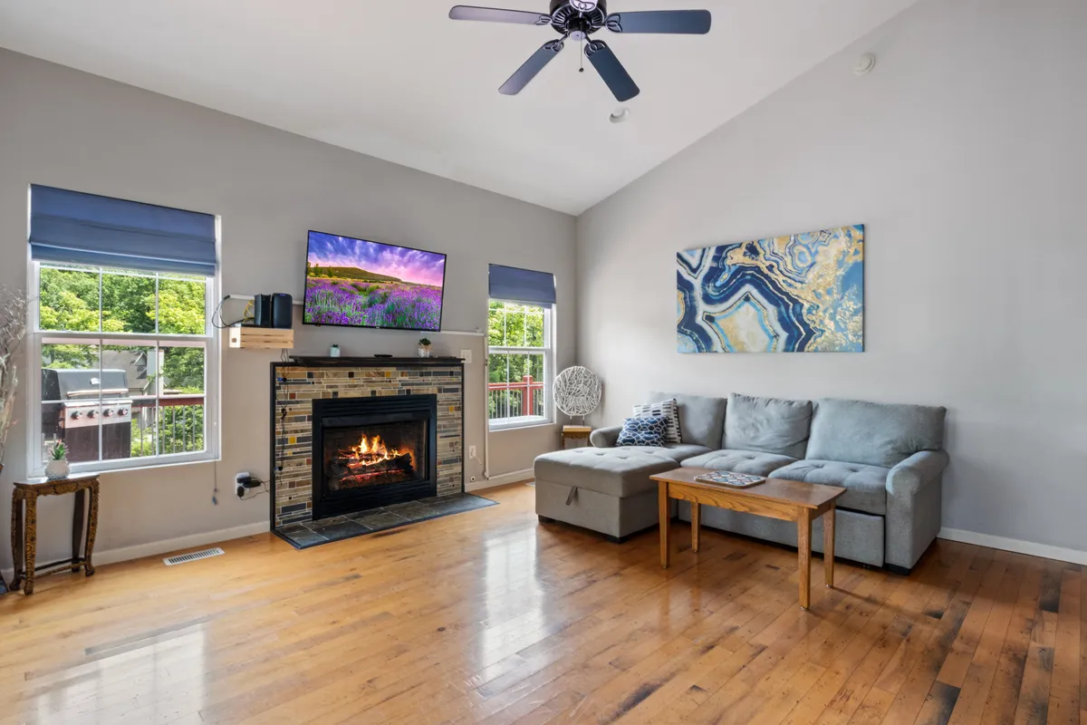 A warmly lit living room featuring a cozy fireplace, a comfortable sofa, stylish artwork, and a television. The windows allow for natural light while maintaining a sense of privacy and comfort. The space feels inviting and secure, ideal for relaxing or spending time with loved ones.