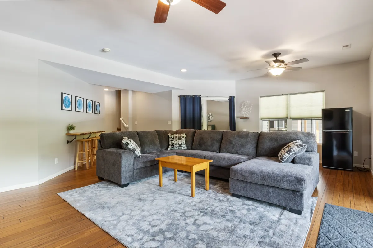 This image features a large sectional sofa arranged around a wooden coffee table, complemented by framed wall art and a ceiling fan. The space is designed for relaxation and conversation, with an open, social layout ideal for group gatherings.
