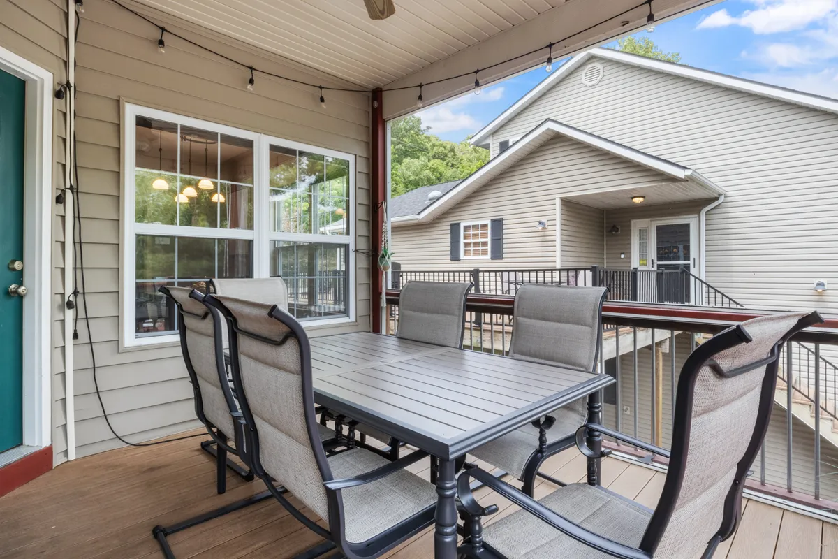 An outdoor dining area nestled amidst lush greenery with string lights overhead, centering on a large dining table ideal for group gatherings. This inviting space emphasizes opportunities for outdoor meals and socializing while enjoying the natural surroundings near the lake.